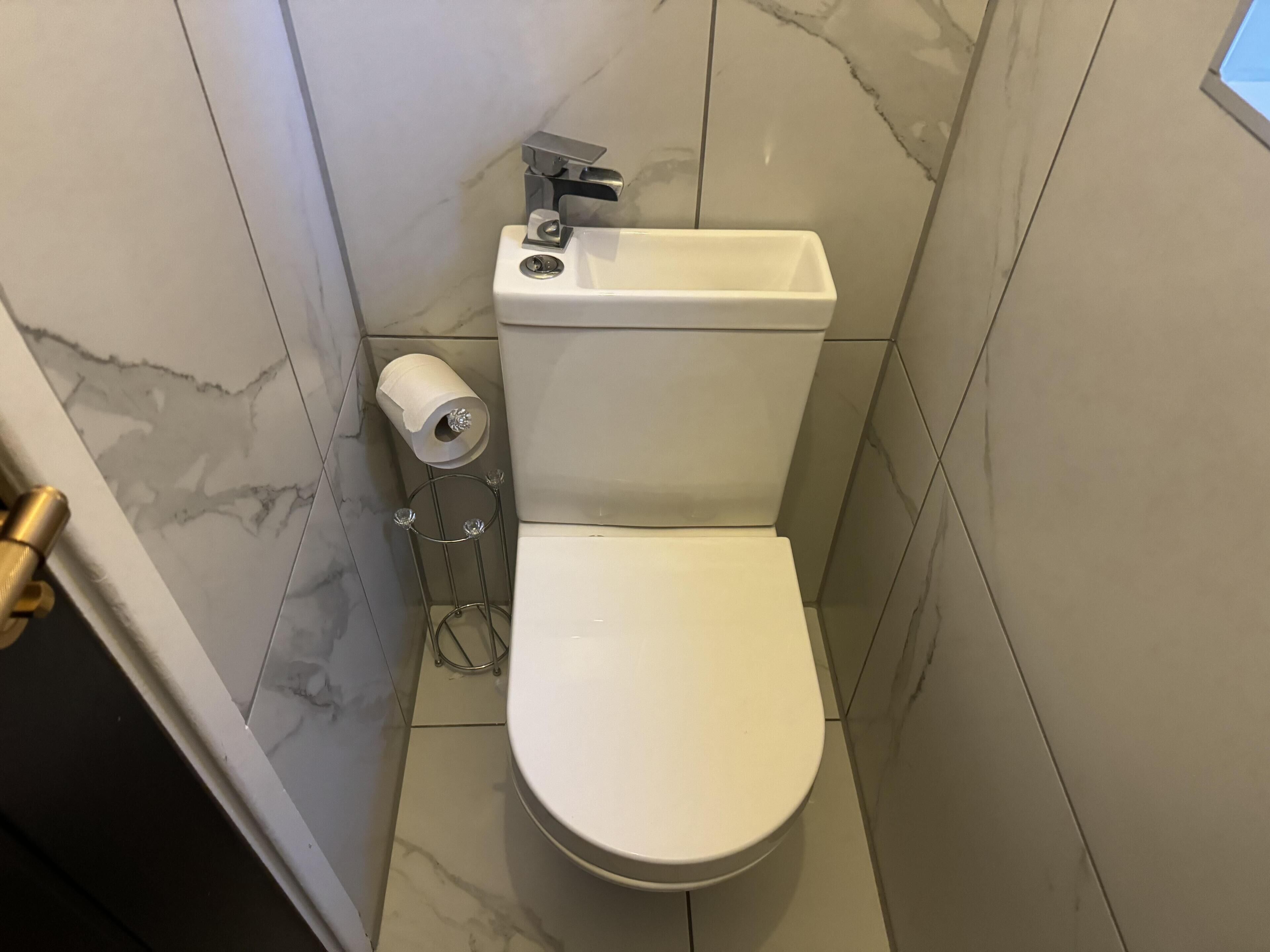 Des toilettes blanches, dotées d’une poignée de chasse d’eau et d’un porte-rouleau de papier toilette.