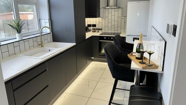 A modern kitchen with a built-in oven, a sink, and a bar area with a bottle of champagne and glasses. - Impeccable 3-bed House in Walsall (Walsall)