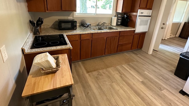 Een moderne keuken met houten kastjes, een granieten aanrecht, een ingebouwde magnetron, een kookplaat, een spoelbak en een raam dat voor daglicht zorgt.