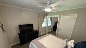 Een slaapkamer met een bed, een dressoir, een televisie en een plafondventilator.