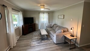 Een woonkamer met een televisie, bank, salontafel en plafondventilator.