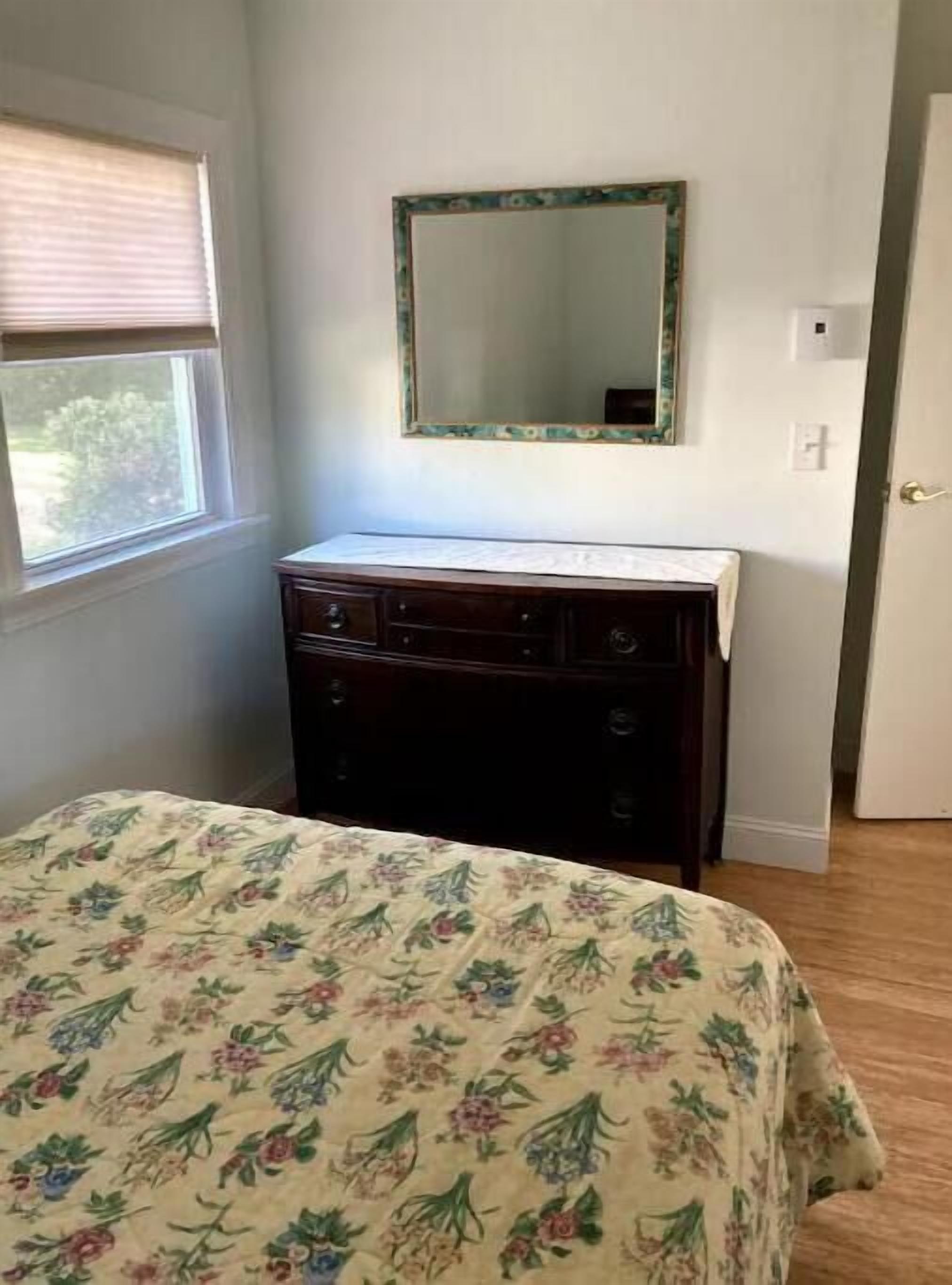A bedroom with a bed, a dresser, a mirror, and a window.