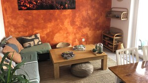 Ein gemütliches Wohnzimmer mit Couch, Holztisch, bunten Kissen, einer hängenden Lampenschirm und einem Wandregal mit Dekoration.
