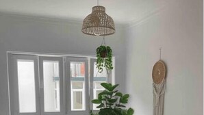 Ein Schlafzimmer mit einem Bett, Nachttischen, einer hängenden Pflanze, einer Wanddeko aus Makramee und einem Fenster mit weißen Rahmen.