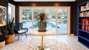 A modern living room with a pool view, a round table with a plant, a bookshelf, and a chair. - Heated Pool, Hot Tub & Mountain Views on 15 Acres! New Listing Special! (Freehold)