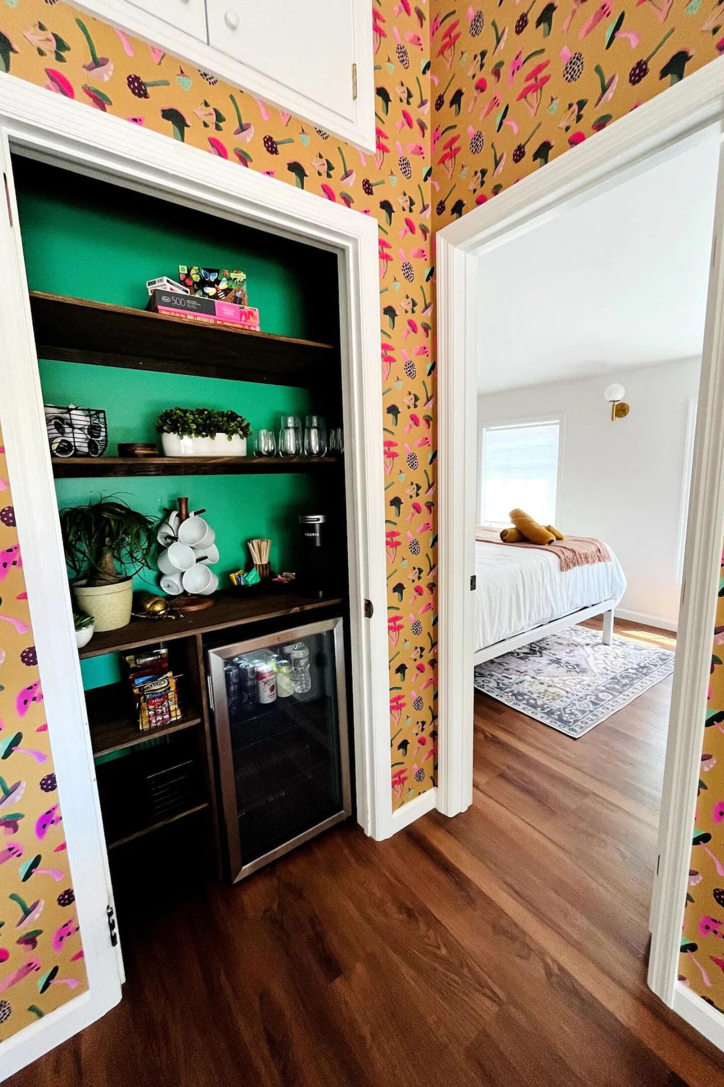 Una habitación con cama, una kitchenette pequeña y un estante verde.