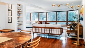 A modern living room with a wooden dining table, a white sofa, and a large window with a view of trees. - Heated Pool, Hot Tub & Mountain Views on 15 Acres! New Listing Special! (Freehold)