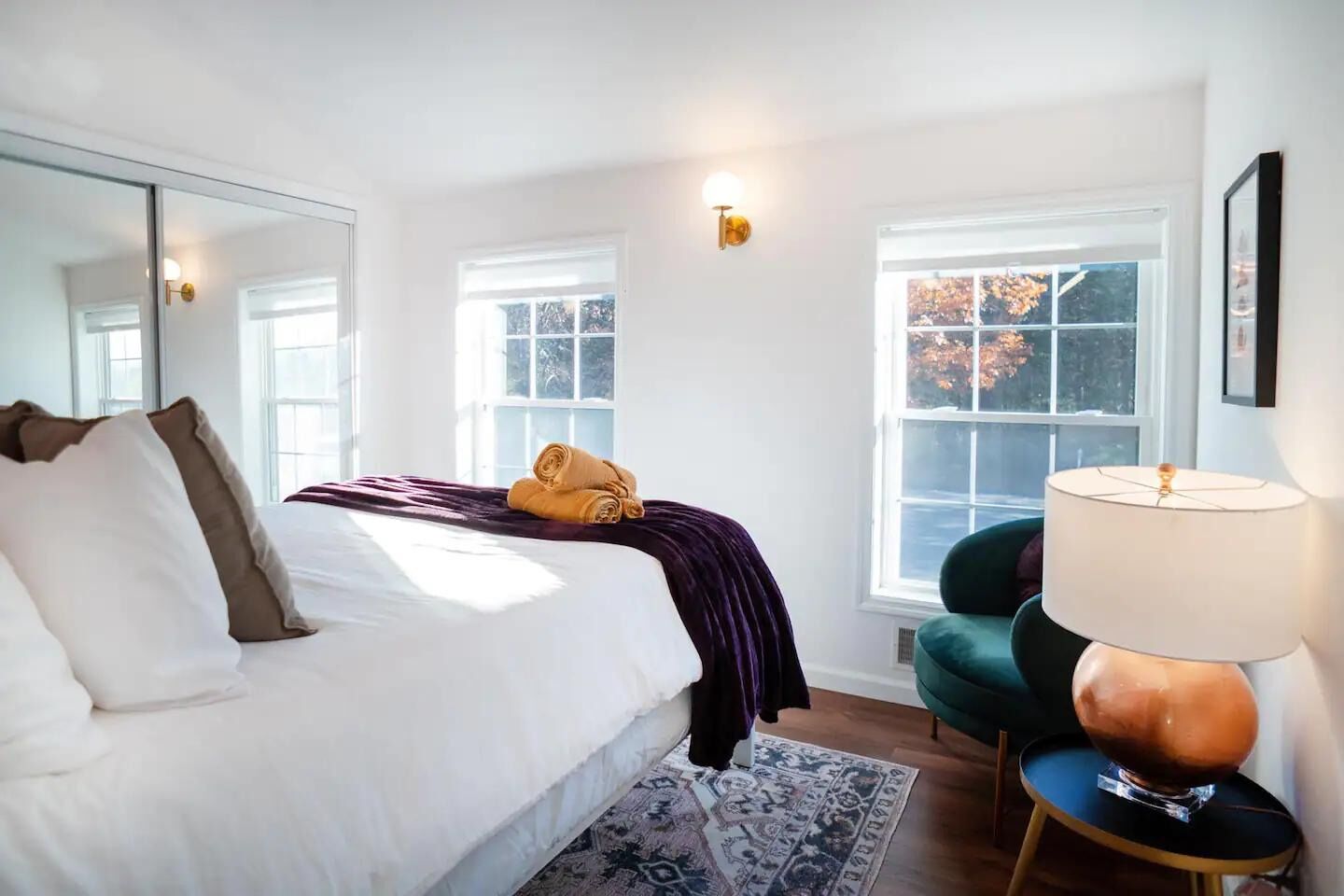 Un dormitorio con cama, dos ventanas, una lámpara y una silla.
