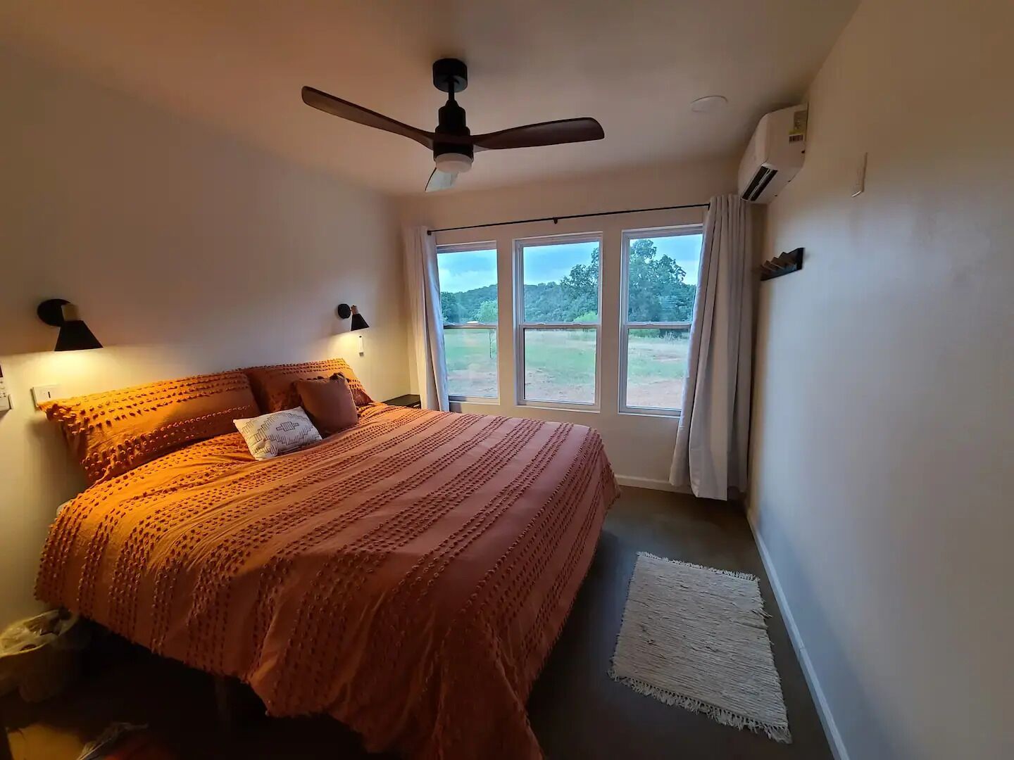 A bedroom with a large bed, a ceiling fan, and a view of the outdoors through a window.