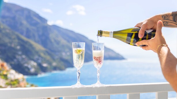 A person pouring champagne into two glasses on a balcony with a scenic ocean view. - Adoro Positano (Positano)