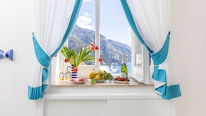 A kitchen with a view of mountains through a window, a vase with flowers, and a bottle of wine on the counter. - Adoro Positano (Positano)