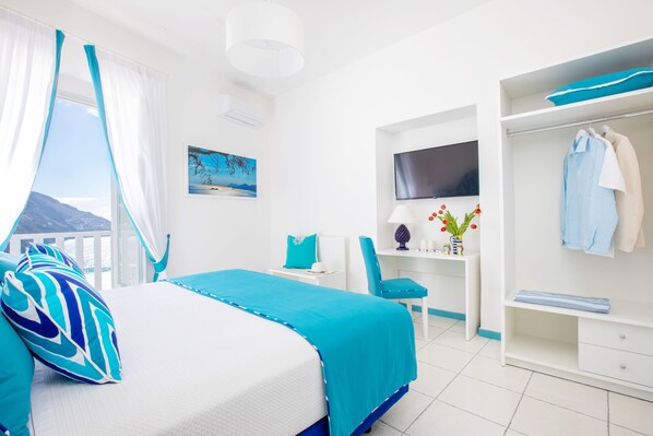 A hotel room with a bed, a desk, a chair, a TV, and a wardrobe. - Adoro Positano (Positano)