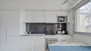 A modern kitchen with white cabinets, a black tiled backsplash, and a window providing a view of the outside.