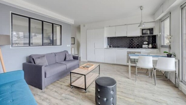 A modern living room with a grey sofa, a coffee table, and a dining area with white chairs.