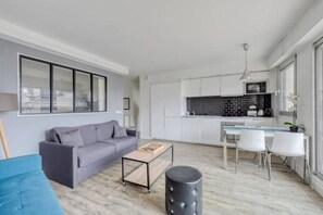 A modern living room with a grey sofa, a coffee table, and a dining area with white chairs. - Charming apartment between Paris and EuroDisney (Nogent-sur-Marne)
