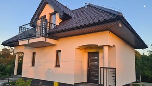 A two-story house with a balcony, a front door, and a small garden area.