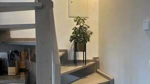 A kitchen with a built-in oven and a countertop with utensils. There is a plant on a small table next to a staircase.