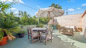 An outdoor patio with a wooden table and chairs, a striped umbrella, and potted plants.