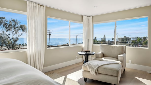 A bedroom with a large window, a bed, a chair, and a small table.