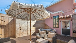 An outdoor patio with wicker furniture, a striped umbrella, and a wooden deck.
