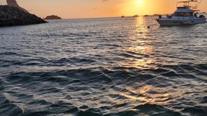 A sunset over a calm sea with a rocky outcrop on the left and a boat on the right. - Pousada Shalon Adonai Noronha (Fernando de Noronha)