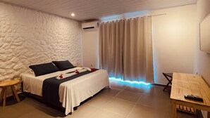 A modern bedroom with a bed, a wooden table, and a stone-textured wall. - Pousada Shalon Adonai Noronha (Fernando de Noronha)