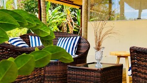 A wooden deck with wicker furniture, including chairs and a table, surrounded by lush greenery. - Pousada Shalon Adonai Noronha (Fernando de Noronha)