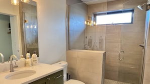 A modern bathroom with a glass shower enclosure, a toilet, and a sink with a mirror above it. - Tranquility Base, Modern One-Bedroom Apartment (Carbondale)