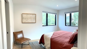 A bedroom with a bed, a chair, two windows, and a wall art piece. - Tranquility Base, Modern One-Bedroom Apartment (Carbondale)