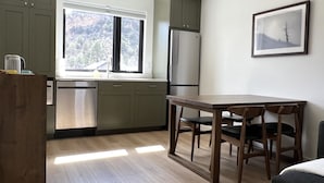 A modern kitchen with a built-in dishwasher, a stainless steel refrigerator, and a window overlooking a forested area. - Tranquility Base, Modern One-Bedroom Apartment (Carbondale)