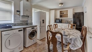 A compact kitchen with a built-in washer and dryer, a dining table with chairs, and a refrigerator. - 3-bed House, Sleeps 6, Free Parking,wifi (Basildon)