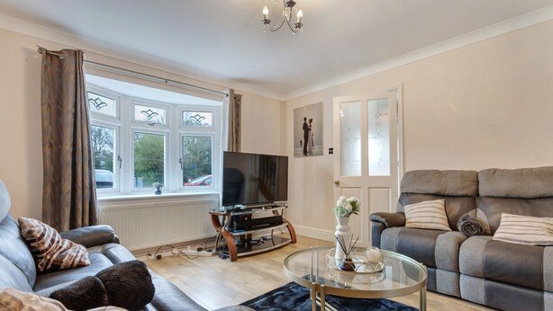 A living room with a sofa, a glass coffee table, a TV on a wooden stand, and a large window with curtains. - 3-bed House, Sleeps 6, Free Parking,wifi (Basildon)