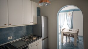 A modern kitchen with white cabinets, a stainless steel refrigerator, and a sink. There is a dining table with chairs in the background through an archway. - Casa Belmonte (Como)