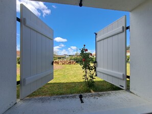 An open door leading to a grassy area with a rose bush and a pile of firewood.