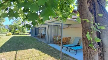 A covered outdoor seating area with tables and chairs, a grassy lawn, and a tree trunk.