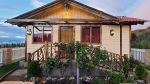 Una casa de madera con un porche delantero, una valla de madera y un jardín con flores y arbustos.
