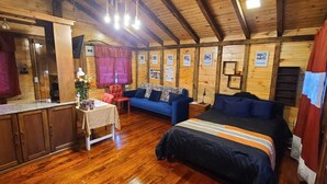 Interior acogedor de una cabaña con piso de madera, un comedor con mesa y sillas, un sofá y una cama con manta a rayas.