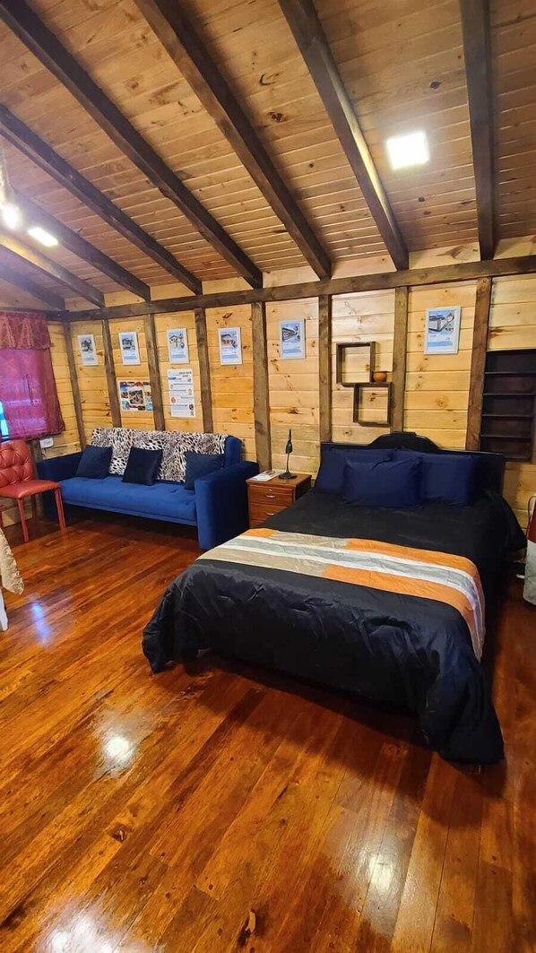 Eine Holzjagdhaus mit einem großen Bett, einem blauen Sofa und einem roten Sessel.