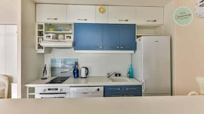 A compact kitchen with white and blue cabinets, a white refrigerator, a sink, and a coffee maker.