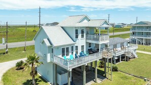A two-story beachfront house with a balcony, outdoor seating, and a small deck area. - Sun, Sand & Surf Await! 3rd House from Beach, Dogs Welcome, Fenced Area, 2 Decks (Galveston)