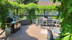 Un patio al aire libre con una parrilla, una zona de estar y vista a una casa al fondo.