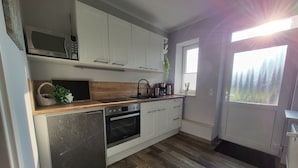 Una cocina compacta con gabinetes blancos, microondas, lavavajillas y cafetera.
