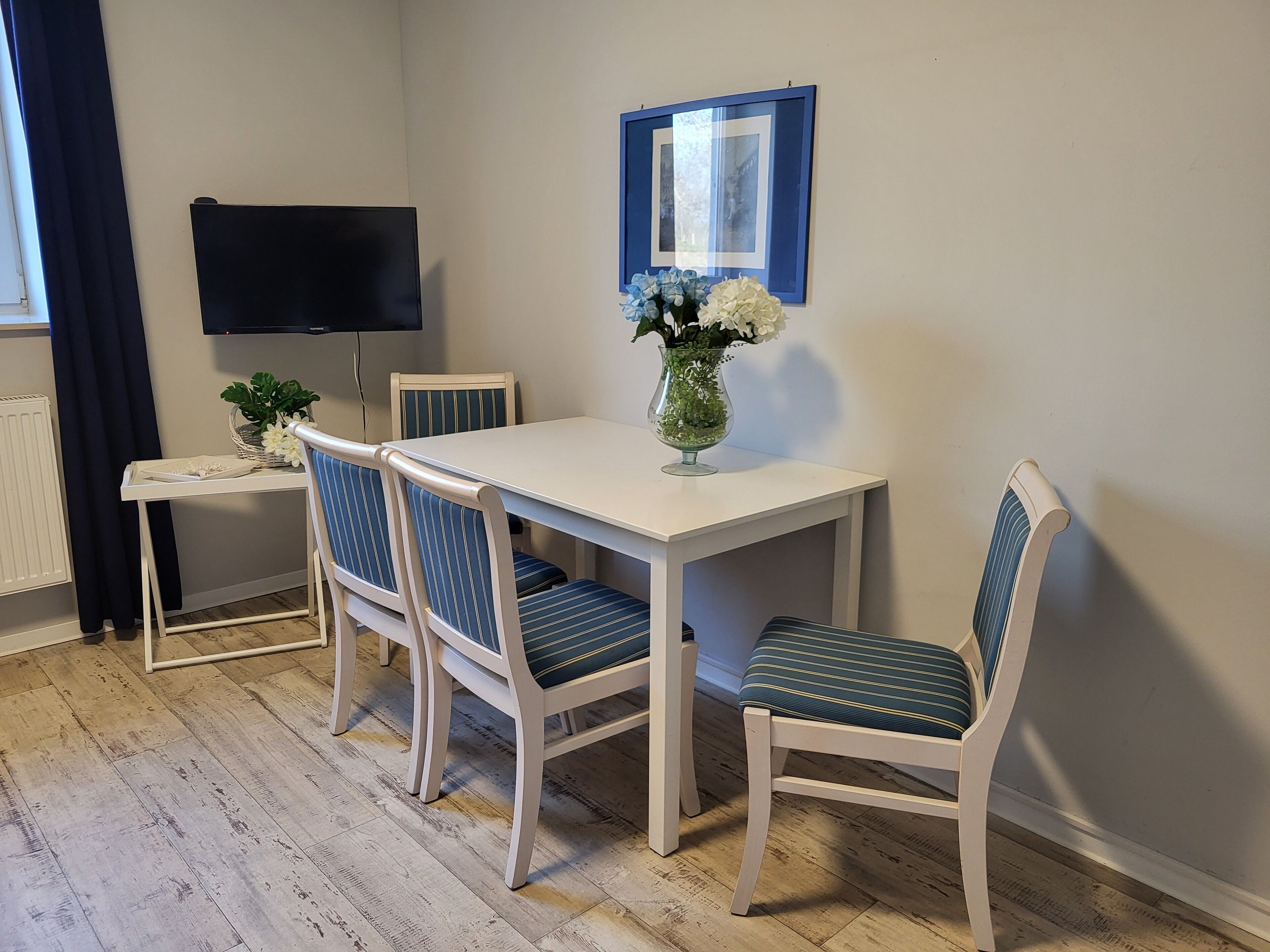A dining area with a white table and four striped chairs, a vase with flowers, and a framed picture on the wall.