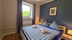 Una cama bien hecha con ropa de cama a cuadros, un cuadro en la pared y una ventana con cortinas.