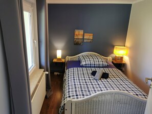 Une chambre à coucher avec un lit, deux lampes de chevet, un radiateur et une fenêtre avec des rideaux.