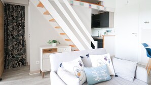 A modern living room with a sofa, pillows, a small white cabinet, and a staircase leading to a kitchen. - Pretty flat with ocean and lake views Les Sables - sleeps 4 (Les Sables-d´Olonne)