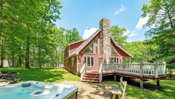 Une cabane avec une cheminée en pierre, un bain à remous et une terrasse en bois.