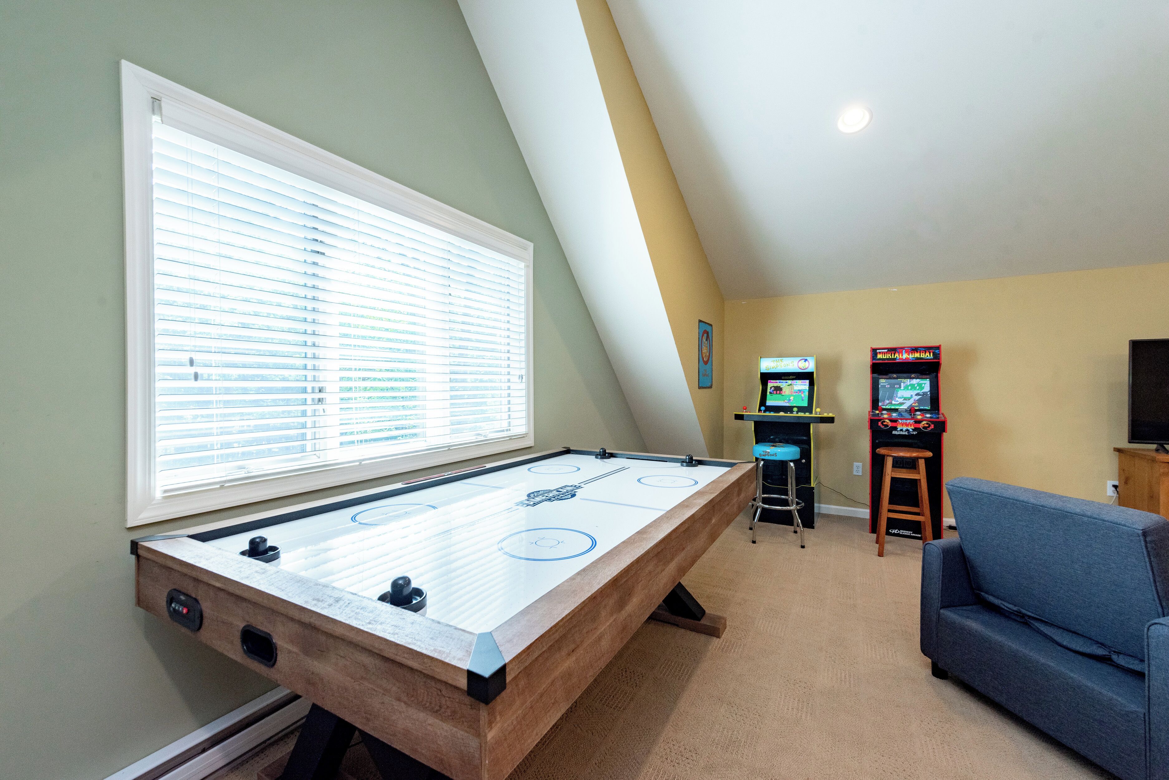 A room with a pool table, a sofa, and two arcade machines.