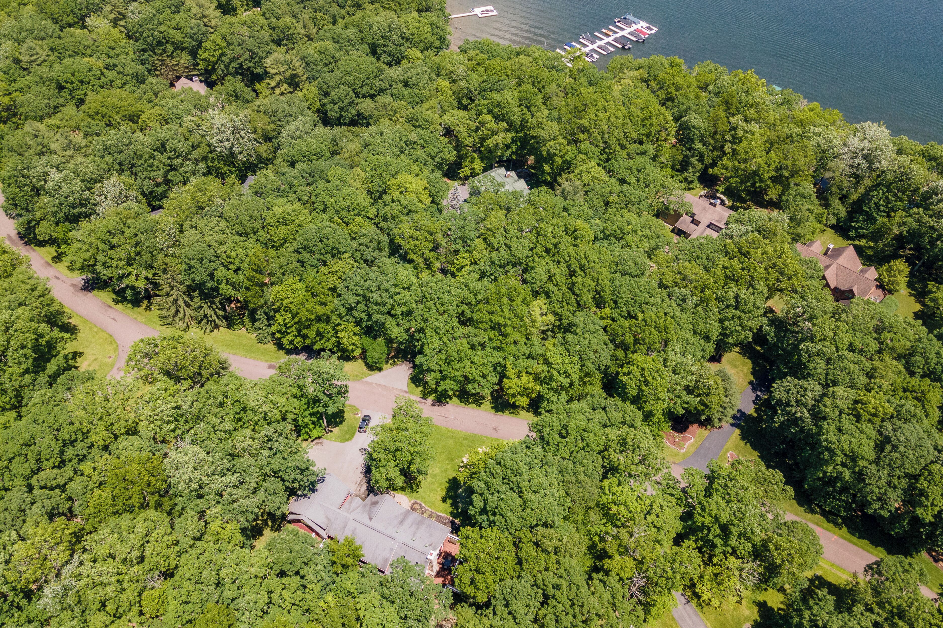 An aerial view of a residential area with multiple houses surrounded by dense greenery and a lake.
