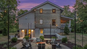 A two-story log cabin with a covered porch, outdoor seating area with chairs and a fire pit, and a stone fireplace. - Luxury Modern Cabin* 5 Acres* Pickle Ball*Hot Tub (Primm Springs)